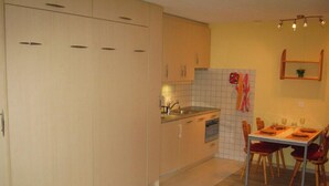 A compact kitchen with a dining area, featuring cabinets, a sink, and a tiled backsplash. - Comfortable Studio for 2-4 persons : Living room with sofa-bed (1.40 x 1.90m) and 2 pull-down beds - (Grimentz)