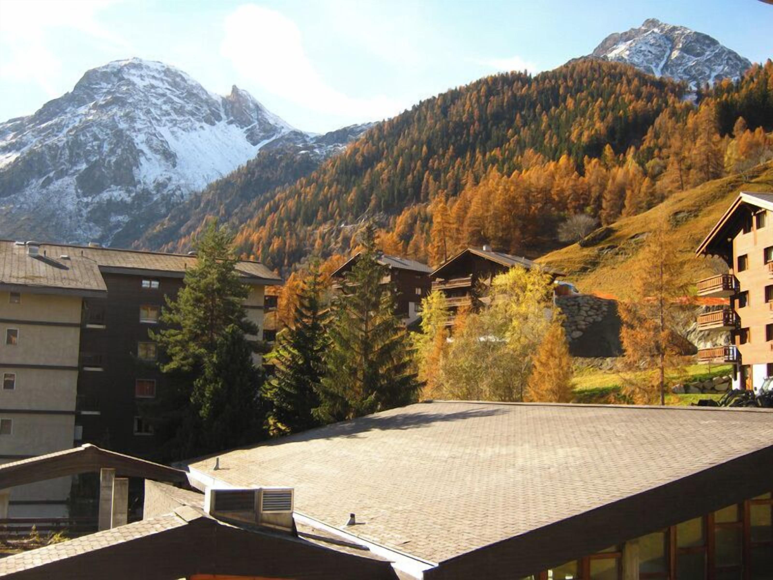 A mountain resort with buildings, a ski slope, and autumn foliage.