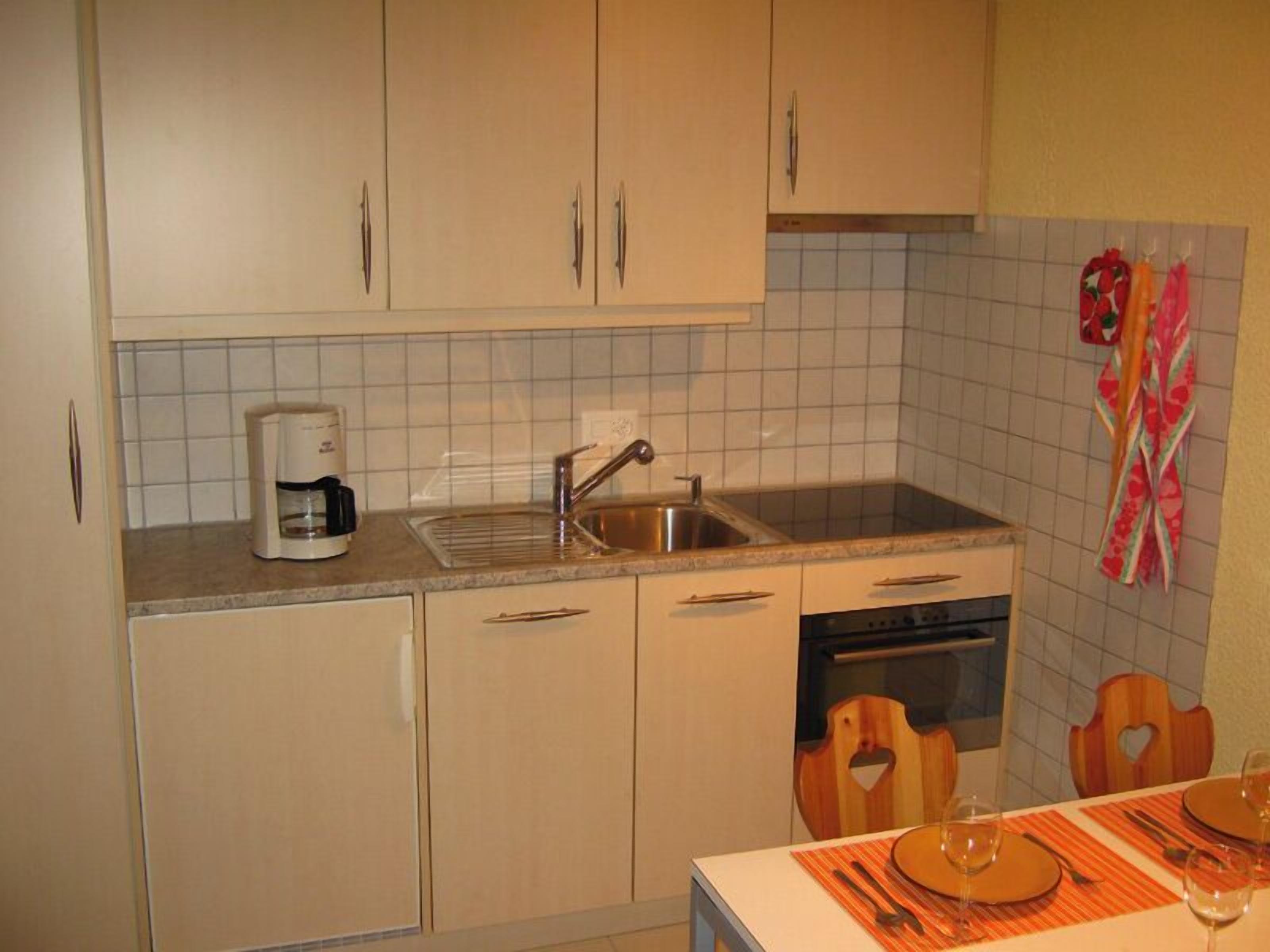 A kitchen with light-colored cabinets, a coffee maker, a sink, and a tiled backsplash.