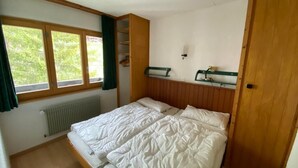 A bedroom with a bed, a radiator, a window with curtains, and a wooden wardrobe. - 2-room apartment for 4 persons : Living room with 2 sofa-beds - 1 room with 2 beds - kitchen with fi (Grimentz)