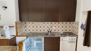 A compact kitchen with dark wooden cabinets, a patterned backsplash, a built-in oven, and a small refrigerator. - 2-room apartment for 4 persons : Living room with 2 sofa-beds - 1 room with 2 beds - kitchen with fi (Grimentz)