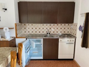 A compact kitchen with dark wooden cabinets, a patterned backsplash, a built-in oven, and a small refrigerator. - 2-room apartment for 4 persons : Living room with 2 sofa-beds - 1 room with 2 beds - kitchen with fi (Grimentz)