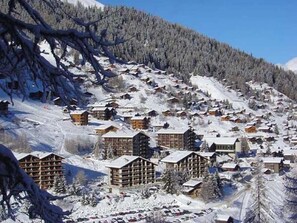 A snow-covered mountain village with wooden buildings, a ski slope, and a clear blue sky. - 2-room apartment for 4 persons : Living room with 2 sofa-beds - 1 room with 2 beds - kitchen with fi (Grimentz)
