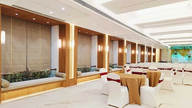 Uma sala de banquetes ampla, com fileiras de cadeiras e mesas brancas, painéis de madeira e iluminação embutida.
