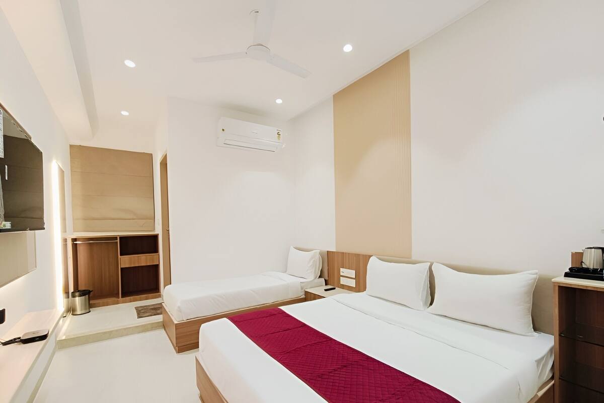 Habitación de hotel moderna con una cama grande, una cama más pequeña, un escritorio, una silla, un armario y un ventilador de techo.