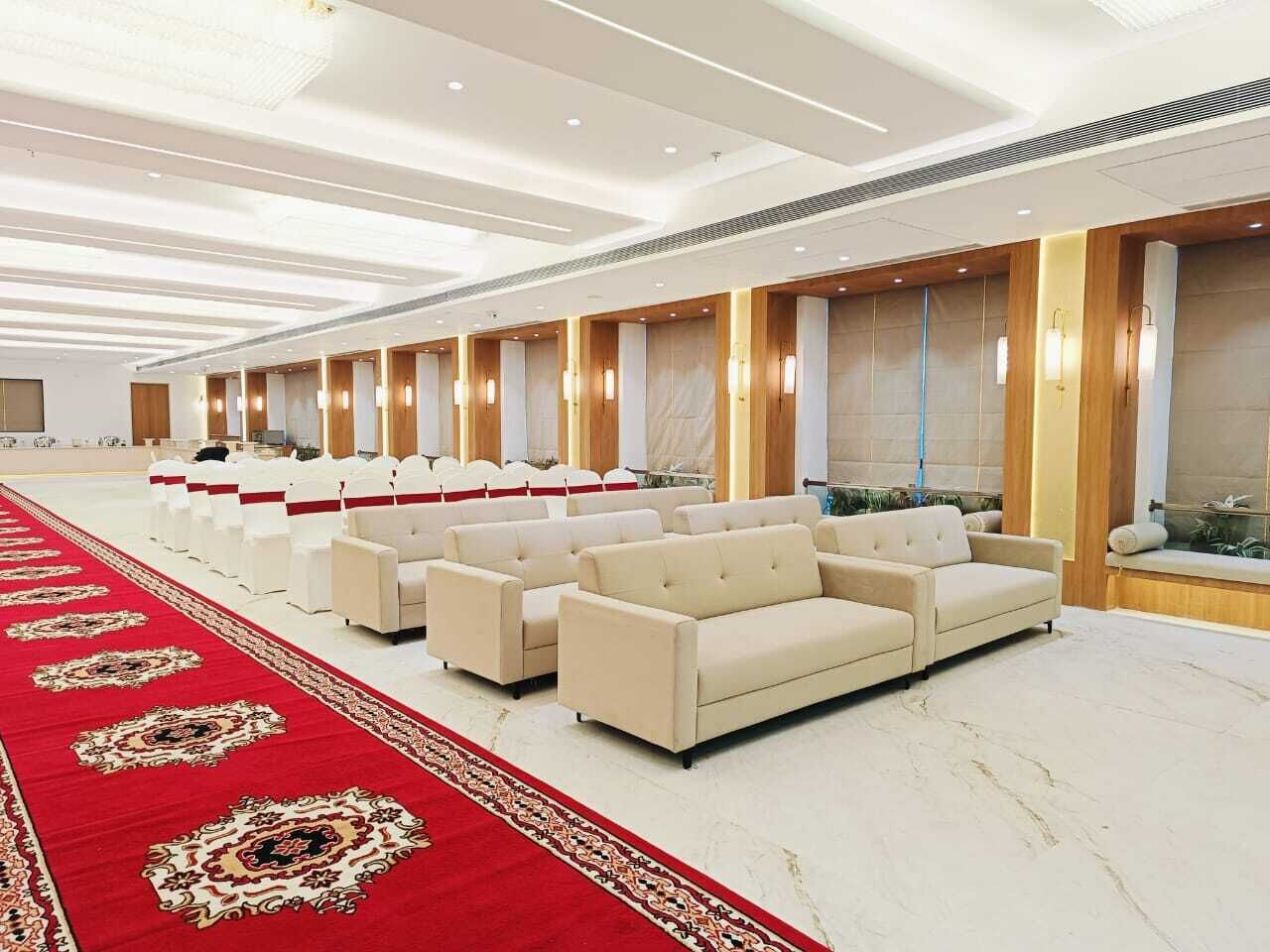 Ein Konferenzraum mit Reihen weißer Stühle, einem roten Teppich und einem beigen Sofa.