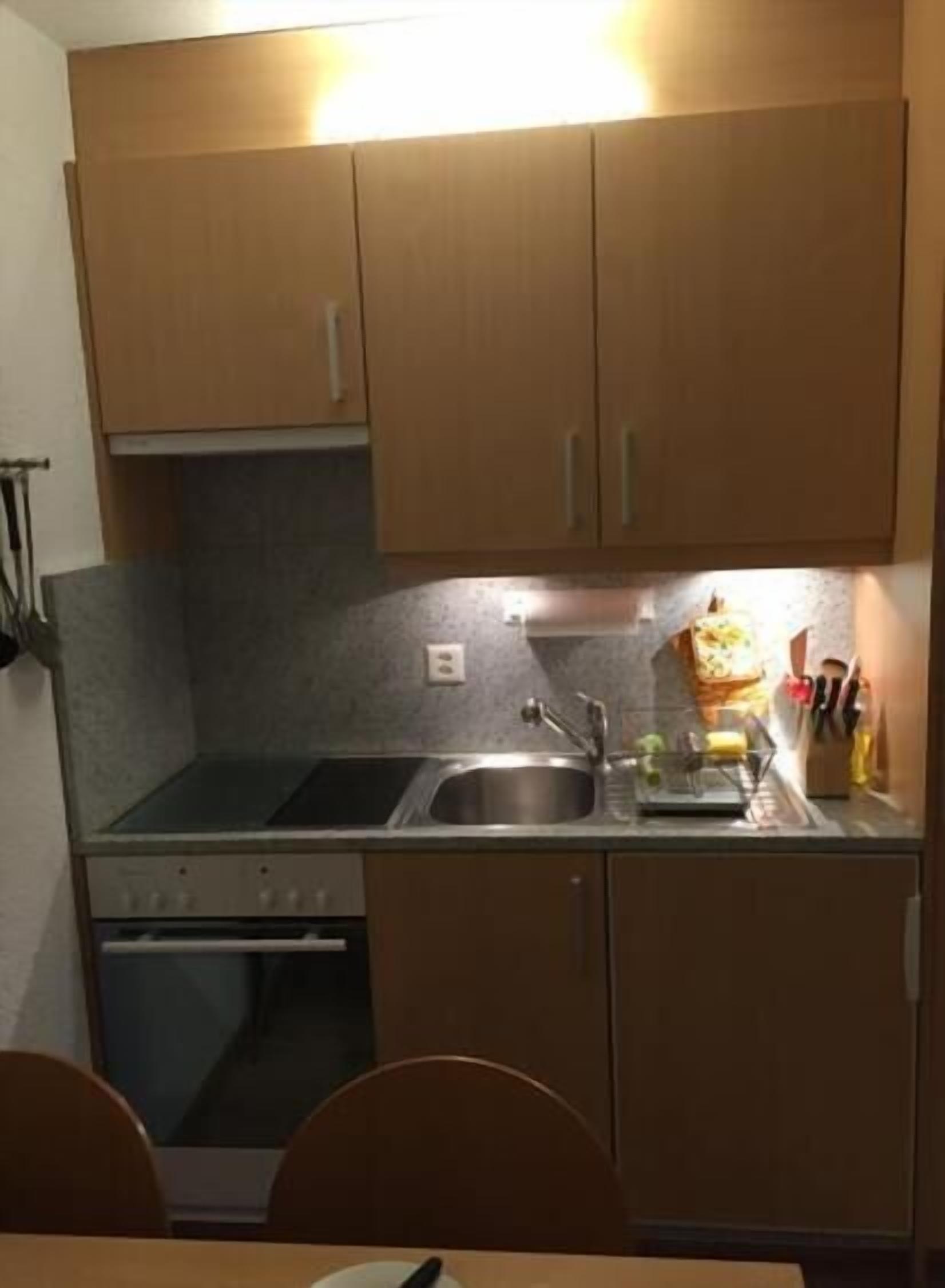 A compact kitchen with wooden cabinets, a stainless steel sink, and a stove.