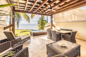 A covered outdoor seating area with wicker furniture, a glass-top table, and a hot tub. - Townhouse With Ocean View Puerto Bahia P5 (Las Terrenas)