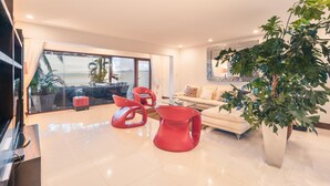 A modern living room with a large window, red chairs, a sofa, and a potted plant. - Townhouse With Ocean View Puerto Bahia P5 (Las Terrenas)