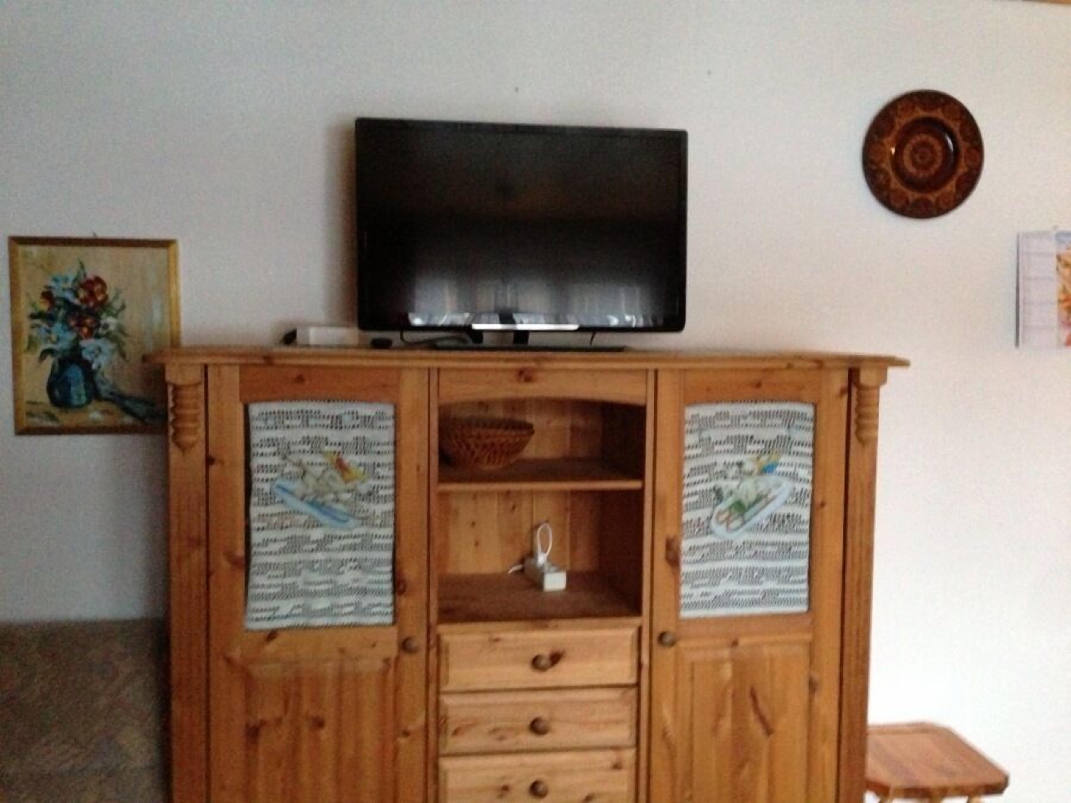 Ein Holzbemöbel-Komponat mit einem Flachbildfernseher obenauf, zwei Ablagen mit dekorativen Papieren und einem kleinen Tisch unten.