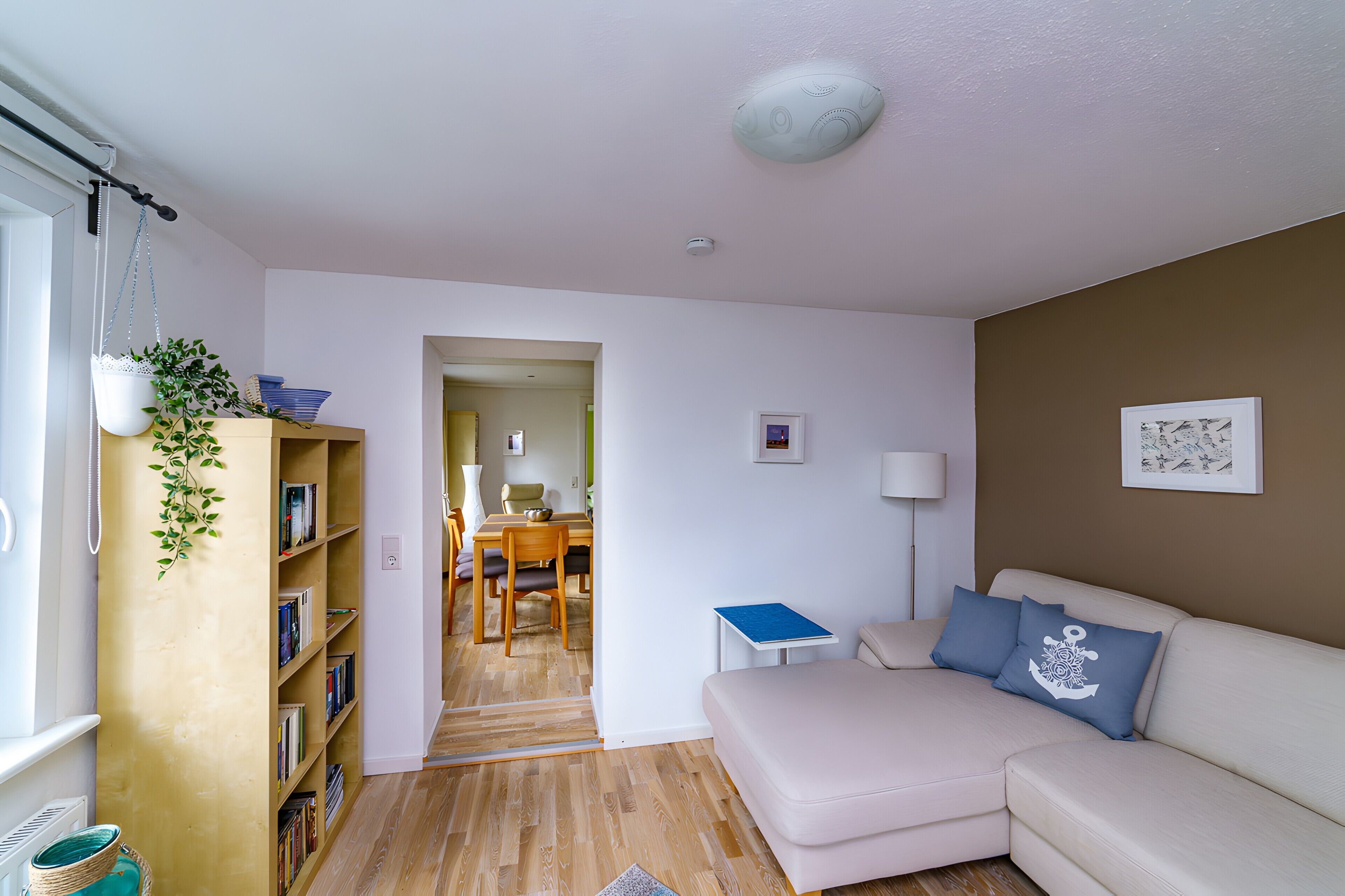 A living room with a sofa, a bookshelf, a dining area, and a hallway leading to another room.
