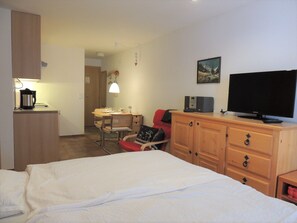 Quarto de hotel com uma cama, uma escrivaninha com cadeira, televisão e guarda-roupa.