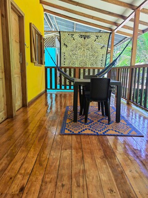 A wooden deck with a table and chairs, a yellow wall, and a view of greenery. - Brisas del Caribe # 2 (Cahuita)