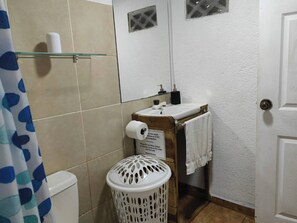 A small bathroom with a toilet, sink, and a white laundry basket. - Brisas del Caribe Apartment (Cahuita)