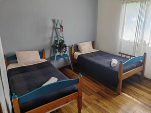 Ein Zimmer mit zwei Holzbett, einer Hockerleiter und einem Fenster mit Vorhängen.