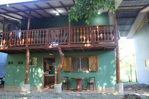 A two-story building with a balcony, a dining area with chairs, and a kitchen visible on the ground floor. - House Number 3 Pura Vida (Cahuita)