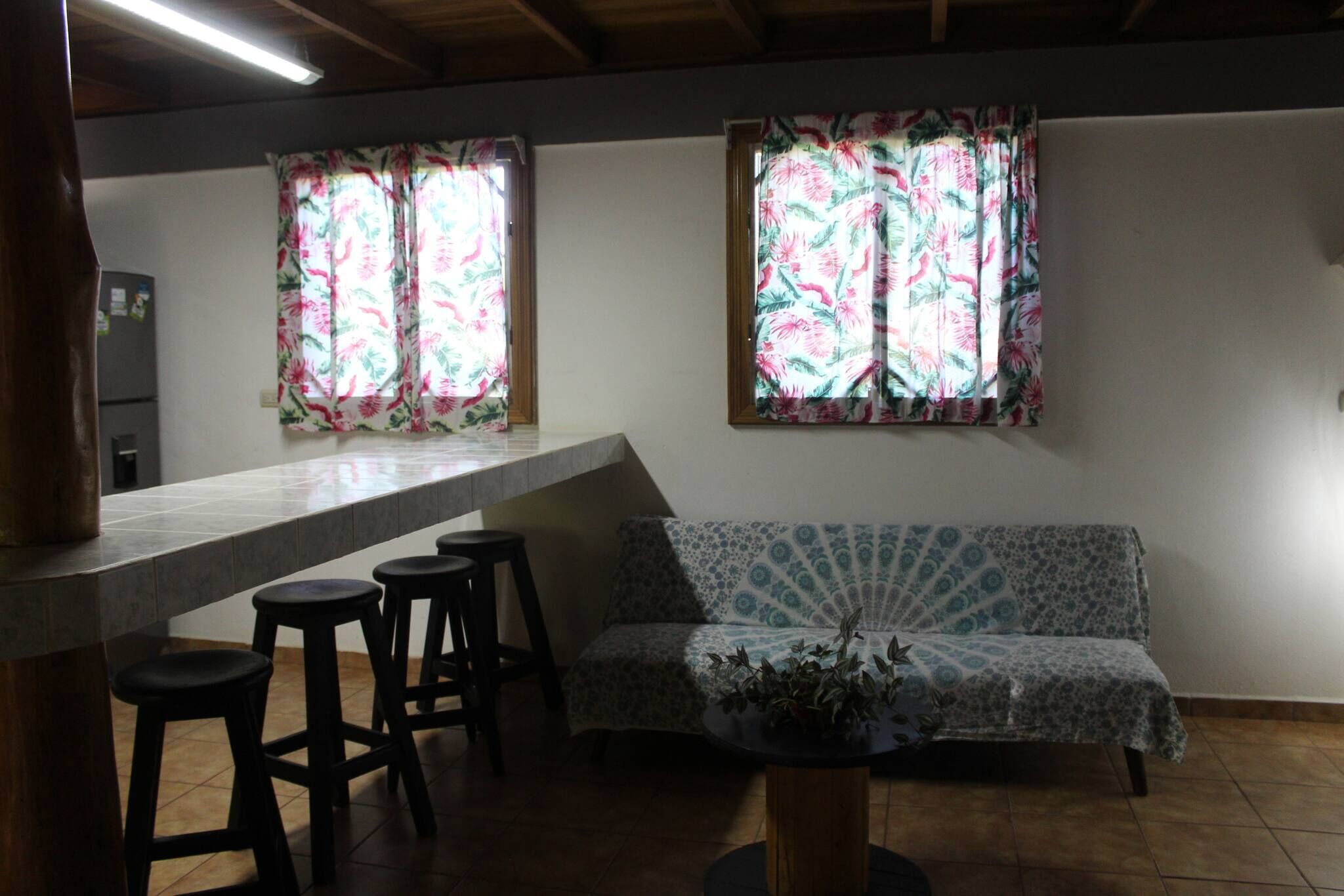 Eine Küche mit Barbereich, einer Couch und zwei Fenstern mit floralen Vorhängen.