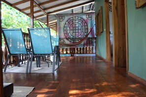 A wooden-floored corridor with a hanging tapestry, two blue chairs, and a view of greenery outside. - House Number 3 Pura Vida (Cahuita)