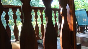 Una terraza de madera con barandilla, un área de estar verde al aire libre y vistas a follaje en el fondo.