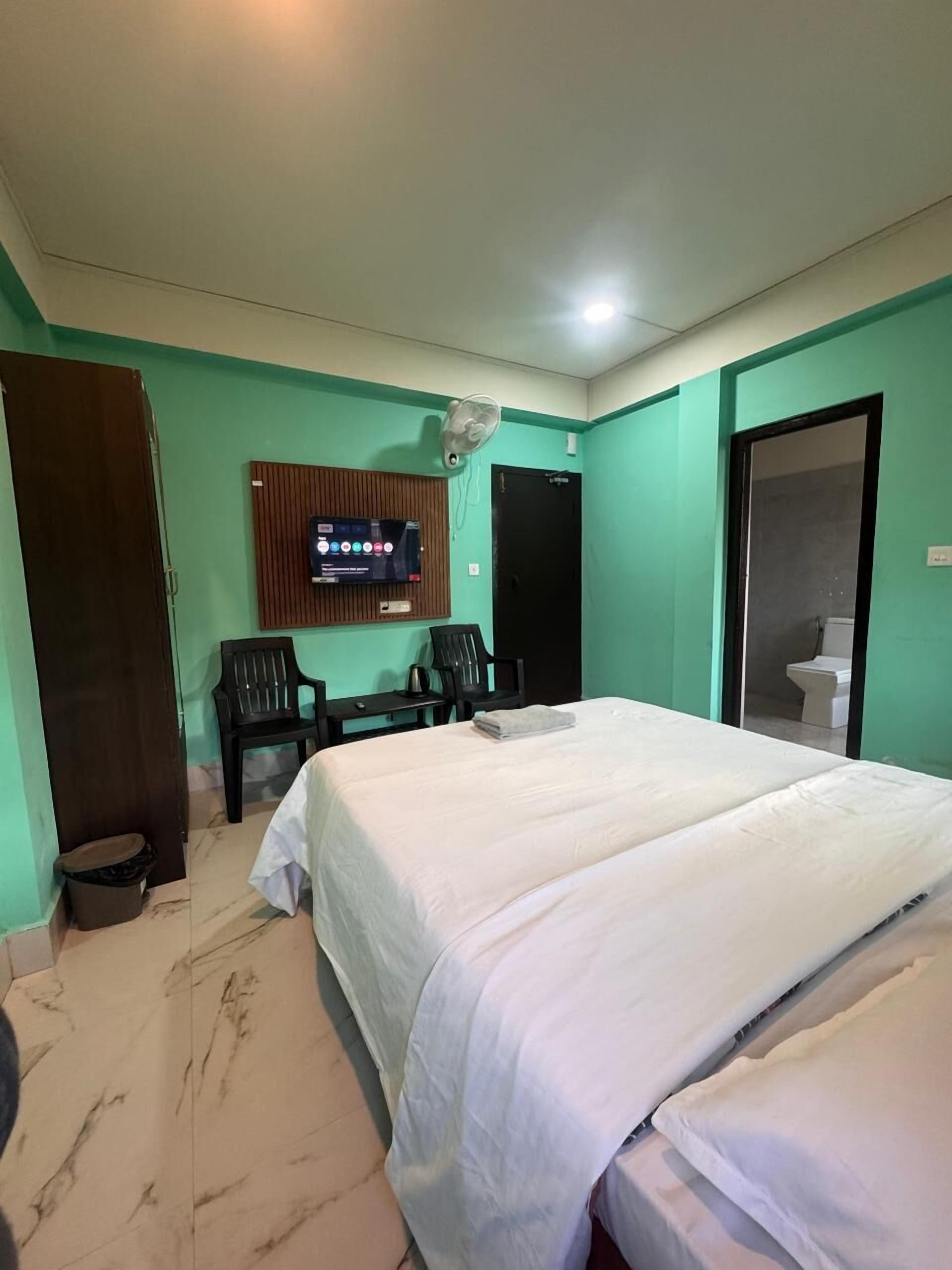 Habitación de hotel con dos camas, un televisor montado en la pared, un escritorio con una silla y una puerta que da a un baño.
