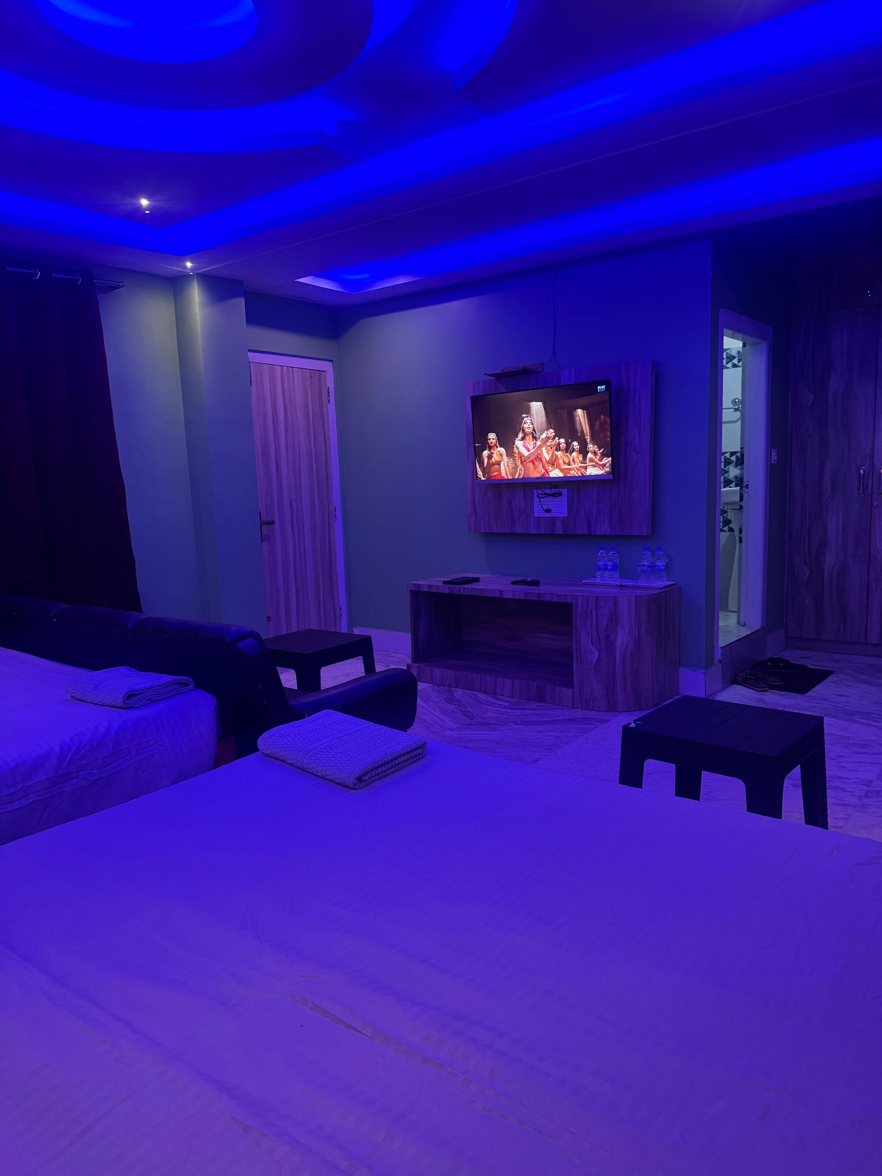 A room with a flat-screen TV mounted on the wall, a wooden cabinet below it, and a bed with a headboard.
