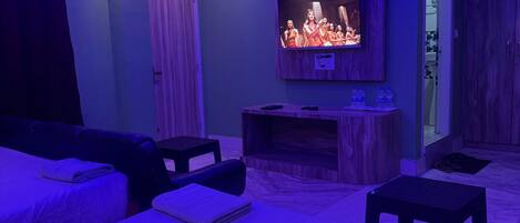 A room with a flat-screen TV mounted on the wall, a wooden cabinet below it, and a bed with a headboard.