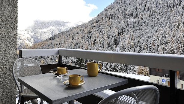 Ein Balkon mit Tisch und Stühlen mit Blick auf einen schneebedeckten Berg und eine Seilbahn.