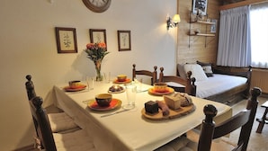 Ein Esstisch ist gedeckt mit Tellern, Schüsseln und einem Blumenstrauß. Im Hintergrund sieht man ein Bett mit weißer Bettdecke und Kissen.