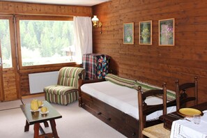Ett mysigt rum med en säng i trä, en randig fåtölj, ett litet bord med en vattenkokare och koppar, och inramade tavlor på väggen.