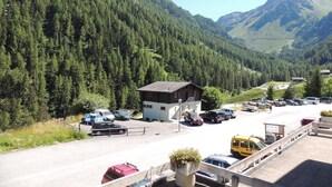 Un estacionamiento con vehículos, un edificio pequeño y un paisaje montañoso.