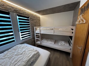 Quarto com beliche, guarda-roupa de madeira, janela com persianas e parede de pedra.