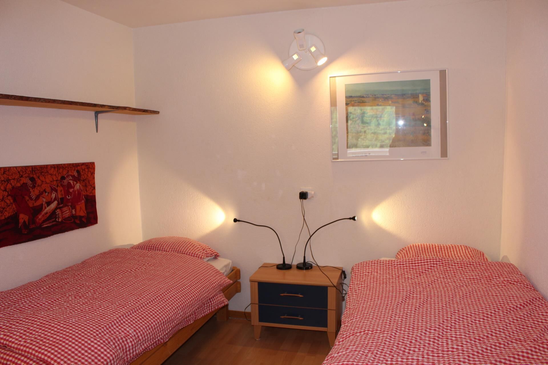 A room with two single beds, a small wooden nightstand, a painting, and a framed picture on the wall.
