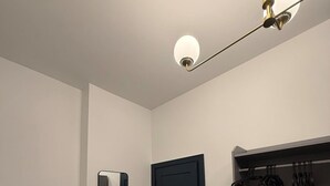 A room with a green chair, a black door, a mirror, a red lamp, and a gray cabinet with hanging items. - Luxury 2 5 Bedroom Flat in Southsea (Portsmouth)