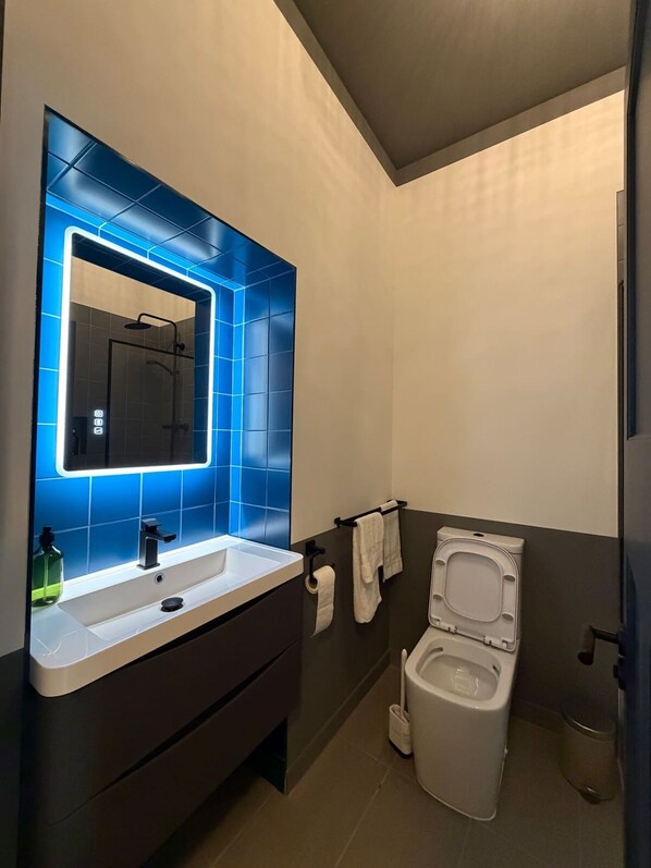 A modern bathroom with a blue-tiled shower enclosure, a white sink with a mirror, and a white toilet. - Luxury 2 5 Bedroom Flat in Southsea (Portsmouth)