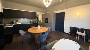 A modern kitchen with dark cabinets, a central island, and a dining area with a round table and chairs. - Luxury 2 5 Bedroom Flat in Southsea (Portsmouth)