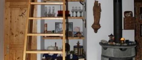 Ein rustikales Interieur mit einer Holzleiter, Regalen voller Gegenstände, einem Kamin und einer Steinwand.