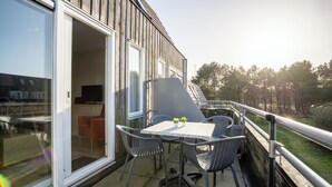 Ein Balkon mit Tisch und Stühlen, eine Schiebetür und Blick auf einen Wald.