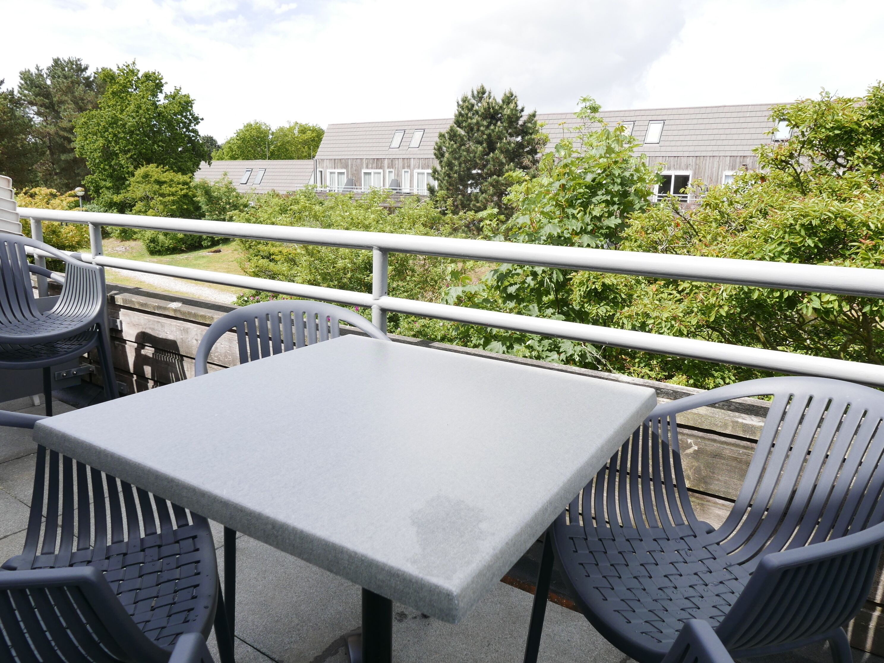 Een terras met een tafel en stoelen, een leuning en uitzicht op gebouwen en bomen.