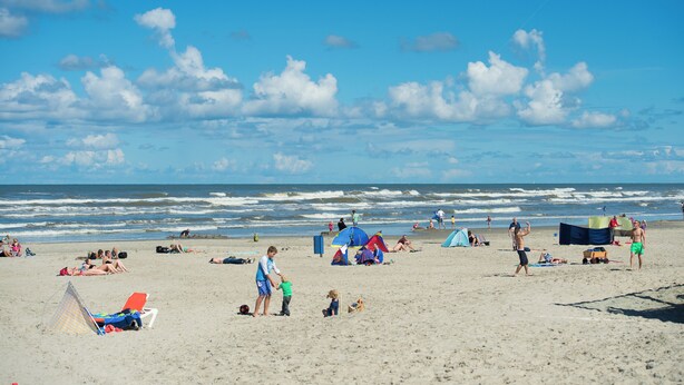 Ein Strand mit entspannten Menschen und einem roten Drachen am Himmel.