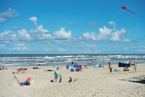 A beach with people relaxing and a red kite flying.