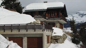 Eine Chalet mit Holzbalkon und Steinunterbau, umgeben von schneebedeckten Bergen.