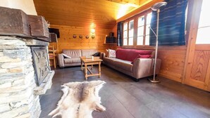 Ein gemütliches Blockhaus-Interieur mit Kamin aus Stein, Ledersofa und Fellteppich.