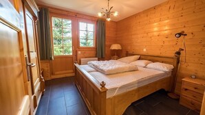 Ein Schlafzimmer mit Holzwandverkleidung, einem Bett, einem Nachttisch, einer Lampe und einem Fenster mit Vorhängen.
