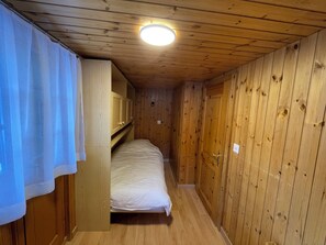 A narrow wooden room with a bunk bed, wooden walls, and a ceiling light. - Comfortable 3 room apartment for 4-6 persons in the old village : Living room with double sofa-bed a (Grimentz)