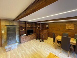 A cozy room with a stone fireplace, wooden shelves, a television, and a dining area with chairs and a table. - Comfortable 3 room apartment for 4-6 persons in the old village : Living room with double sofa-bed a (Grimentz)