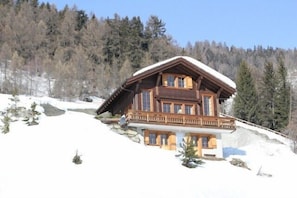 Eine Holzhütte mit Balkon, umgeben von Schnee und Bäumen.