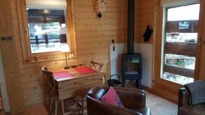 A cozy cabin interior with a wooden interior, a dining table with chairs, a fireplace, and a large window. - Small, very comfortable chalet in the old village for 2 persons : living room with wood-stove - flat (Grimentz)