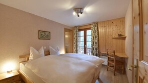 A bedroom with a wooden bed, a bedside table, a chair, and a window with curtains. - Very comfortable 4 room apartment for 6-7 persons : Living room with fireplace - kitchen with dishwa (Grimentz)