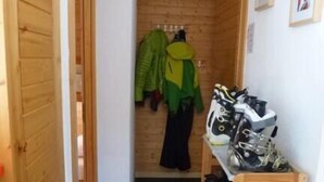 Käytävä, jonka seinät ovat puuta, naulakko, jossa on takkeja, ja kenkäteline, jossa on urheilukenkiä.