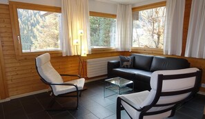A cozy room with a wooden interior, a black leather sofa, white armchairs, and a glass coffee table. - Comfortable 3 room apartment for 4-5 persons : Living room - 1 room with double bed - 1 room with 2 (Grimentz)